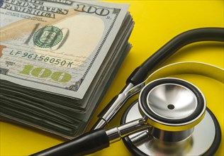 Stack of 100 dollar bills and stethoscope on yellow background