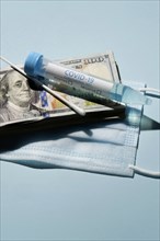 Covid-19 test vial and swab on stack of 100 dollar bills and medical mask