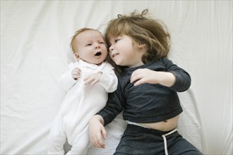 Siblings (2-5 months, 2-3) lying on bed