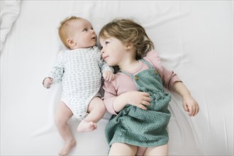 Siblings (2-5 months, 2-3) lying on bed