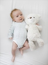 Baby boy (2-5 months) lying on bed with teddy bear