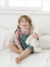 Girl (2-3) sitting on bed with teddy bear