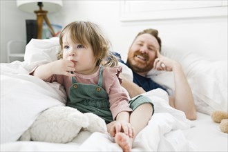 Daughter (2-3) and father watching TV in bed