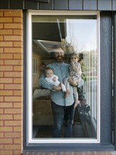 Father with children (2-5 months, 2-3) looking through window