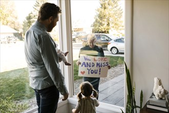 Grandfather showing message to family with grandchildren (2-3 months, 2-3) through window