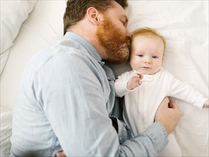 Father kissing baby boy (2-3 months) while lying on bed