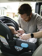 Father buckling baby boy (2-3 months) in car seat