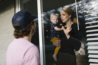 Mother with daughter (2-3) talking to man through window