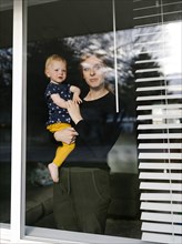 Mother holding daughter (2-3) and looking through window