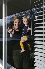 Mother and daughter (2-3) waving through window