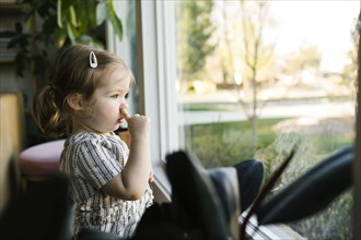 Girl (2-3) picking nose and looking through window