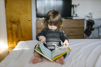 Girl (2-3) reading book on bed
