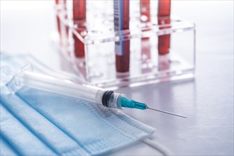 Studio shot of Covid-19 blood samples in test tube rack, syringe and face mask