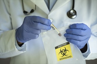 Close-up of doctors hands holding test tube with blood and bag with biohazard sign