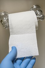 Close-up of hand in blue latex glove reaching for toilet paper