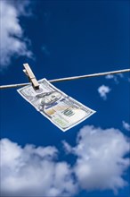 One hundred dollar bill drying on clothesline against sky