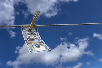 One hundred dollar bill drying on clothesline against sky