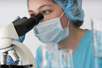 Laboratory technician in face mask looking through microscope