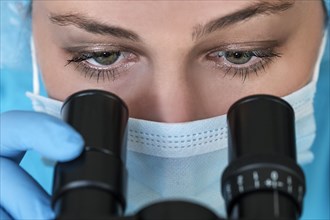 Laboratory technician in face mask looking through microscope