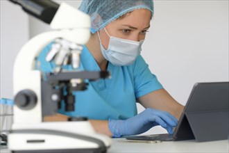 Laboratory technician using tablet next to microscope