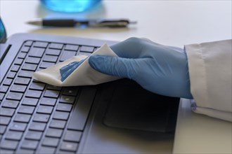 Person wearing blue surgical glove cleaning keyboard of laptop