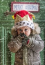 Boy wearing parka and Christmas hat during snowfall in front of green door