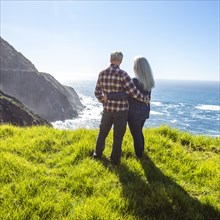 USA, California, Big Sur, Elderly couple watching ocean from grassy cliff
