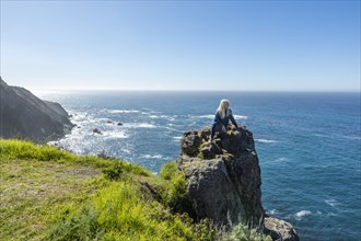 USA, California, Big Sur, Senior woman sitting at the edge of cliff watching view