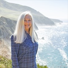 USA, California, Big Sur, Portrait of senior woman against cliffs and sea