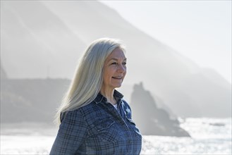 USA, California, Big Sur, Portrait of senior woman in front of cliffs