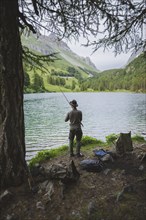 Switzerland, Bravuogn, Palpuognasee, Young man fishing in Palpuognasee lake in Swiss Alps