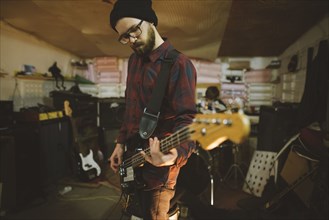 Young man playing bass guitar during rehearsal in garage
