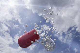 Capsule with white pills inside with clouds as background