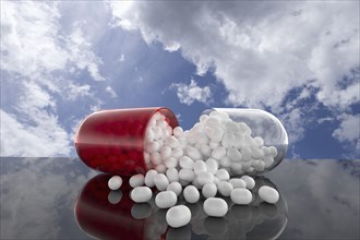 Capsule with white pills inside with clouds as background