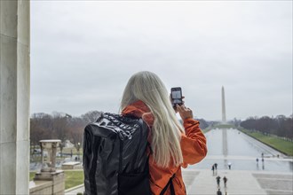 USA, Washington D.C., Tourist takes photo of Washington Monument across pond at National Mall using smartphone