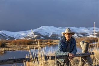 USA, Idaho, Sun Valley, Senior man in cowboy hat leaning against fence