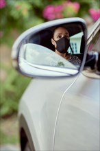 Woman with face mask driving car reflected in mirror