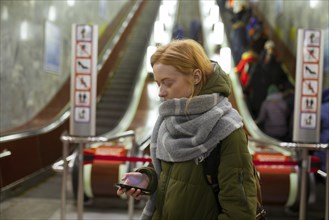 Russia, Novosibirsk, Young woman with smartphone standing by escalator