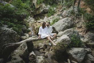 Ukraine, Crimea, Young couple sitting on branch over river in canyon