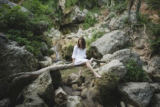 Ukraine, Crimea, Young woman sitting on branch over river in canyon