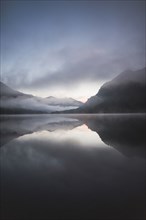 Austria, Plansee, Lake Plansee at sunrise in fog with Austrian Alps