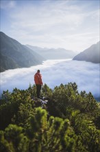 Austria, Plansee, Man standing in trees above valley in clouds in Austrian Alps