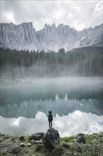 Italy, Carezza, Young man standing and looking at Lago di Carezza in Dolomites