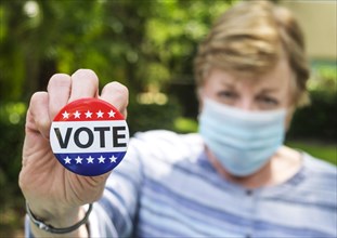 Portrait of woman wearing surgical mask holding Vote button