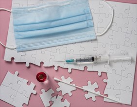 Surgical mask, syringe and vial on white jigsaw puzzle