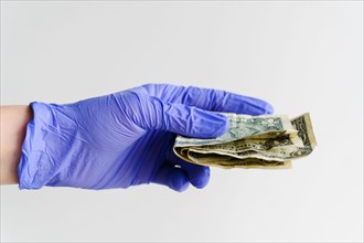 Studio shot of hand in latex glove holding folded dollar bills