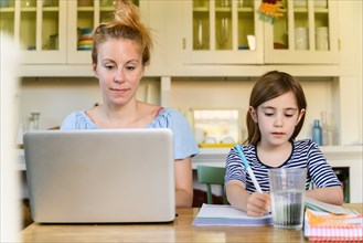 Woman working on laptop and girl (6-7) doing homework