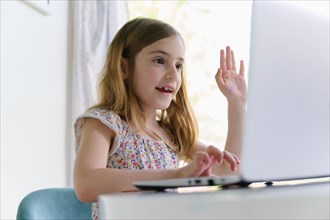 Girl (6-7) waving in front of laptop