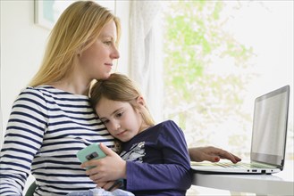 Mother working on laptop while daughter (6-7) using smart phone