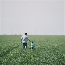 Father with son (2-3) walking across field